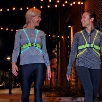 Two woman walking at night and looking at each other, both wearing Tracer2. One tracer is illuminated blue, the other is illuminated green.